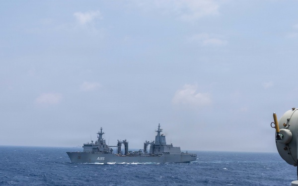 The image shows two naval vessels at sea, photographed from the deck of a third ship. The distant vessel bears the hull number 'A195', identifying it as a naval auxiliary or replenishment ship. A gray optical/fire control sensor system is visible in the foreground on the right side of the frame.