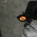 A person wearing black gloves is holding a small black device or tool that contains a circular orange/amber-colored element, possibly a lens, filter, or indicator light. The item appears to be positioned near a vehicle door or panel edge visible on the left side of the frame. The close-up perspective suggests a technical or maintenance activity.