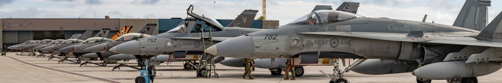 A line of Royal Canadian Air Force (RCAF) CF-18 Hornet fighter jets are parked on a tarmac at a military air base. The aircraft display visible tail numbers including 782 and 757, along with RCAF and 'Canada' markings. Ground crew personnel are visible working around the aircraft.