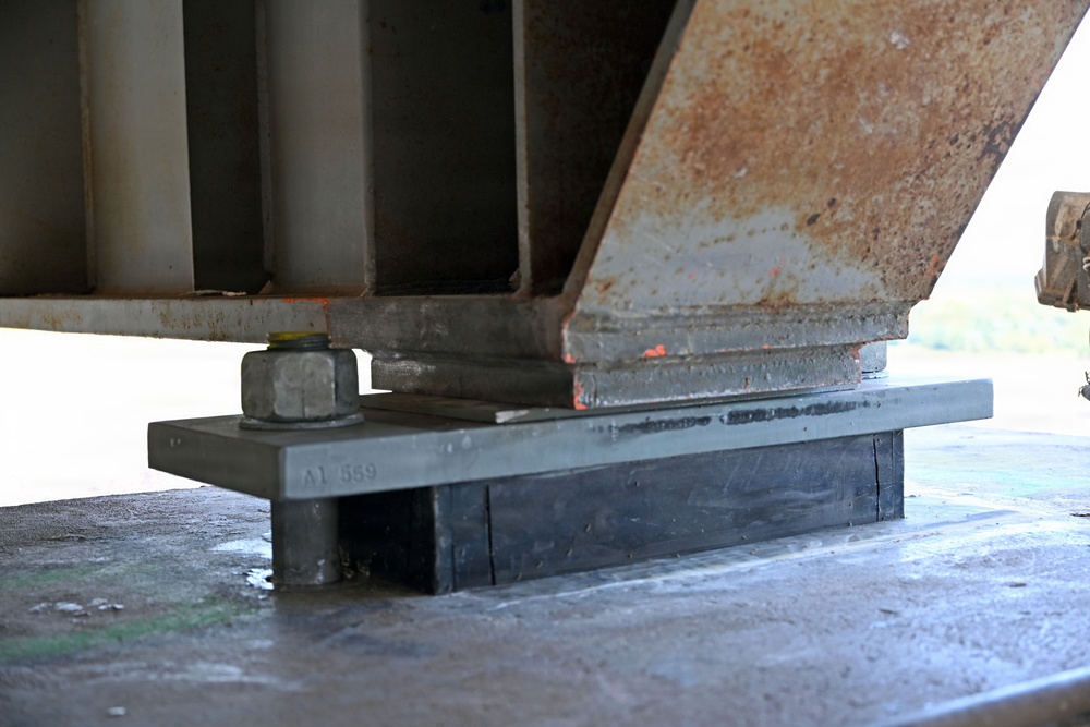 The image shows a close-up view of a bridge bearing assembly, specifically an elastomeric bearing pad supporting a steel girder on a concrete abutment or pier. The bearing pad is marked 'A1 559' and sits beneath a steel sole plate with a visible anchor bolt and nut. Surface rust and minor deterioration are visible on the steel girder components.