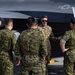 A U.S. Air Force service member in MultiCam/OCP uniform is briefing or conducting a walkthrough with a group of Canadian Armed Forces personnel next to a military aircraft, likely an F-35 or similar stealth jet. The U.S. airman, wearing sunglasses, appears to be explaining features of the aircraft while the Canadian personnel listen attentively. The setting appears to be an outdoor flight line or tarmac.