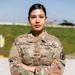 A U.S. Army soldier named Rodriguez stands at ease with arms crossed in an outdoor military setting. She is wearing the standard Army Combat Uniform (ACU) in OCP (Operational Camouflage Pattern) with visible rank insignia of Corporal. The image appears to be a formal or semi-formal portrait taken in daylight.