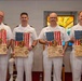 Four U.S. Navy officers in white dress uniforms are posing together while holding wooden plaques featuring the American flag and an official seal. The plaques appear to be certificates from the United States Navy Pastoral Care Residency Program, issued by Naval Medical Center Portsmouth. The setting appears to be a chapel or religious space, indicated by stained glass windows visible in the background.