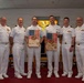 Six U.S. Navy personnel in white dress uniforms pose for a group photo in what appears to be a chapel or religious facility. Two of the individuals are holding wooden plaques featuring American flags and CPEI (Pastoral Care Resiliency Program) insignia. The setting suggests a formal military ceremony or award presentation.