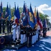A formal military color guard ceremony is taking place outdoors, featuring personnel from multiple U.S. military branches carrying numerous state and organizational flags. The event appears to be connected to a '250' anniversary commemoration, likely related to the United States' 250th anniversary (America250). The ceremony is held on a decorated parade ground or boulevard with a red, white, and blue themed surface.