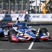 An IndyCar racing car with a patriotic American flag-themed livery sponsored by RE/MAX is competing on a street circuit. The car features red, white, and blue colors with stars and stripes design elements. Spectators and safety barriers are visible in the background along with Boeing and '250' event branding.