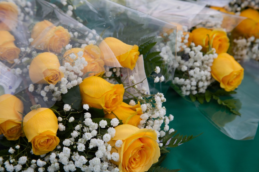 The image shows multiple bouquets of yellow roses accompanied by white baby's breath flowers, wrapped in clear plastic packaging. The bouquets are arranged on what appears to be a teal or turquoise surface, likely a market or retail display. The flowers appear fresh and are presented in a classic florist arrangement style.