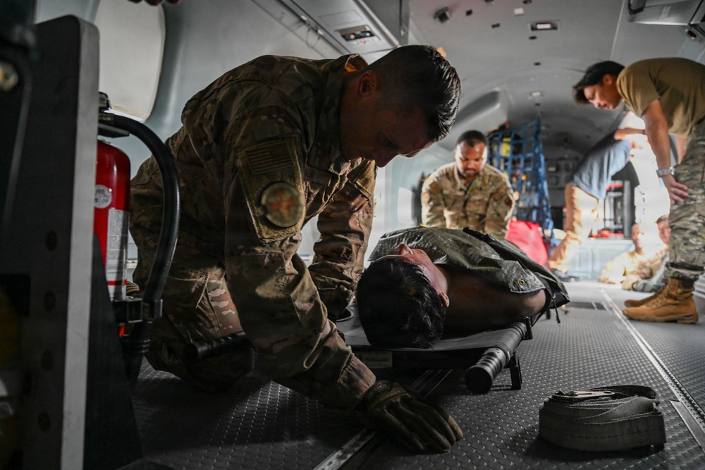 Military personnel in camouflage uniforms are conducting what appears to be a medical evacuation (MEDEVAC) training exercise inside a military aircraft or vehicle. A soldier is attending to a simulated casualty lying on a litter/stretcher on the floor. Additional personnel are visible in the background performing similar tasks.