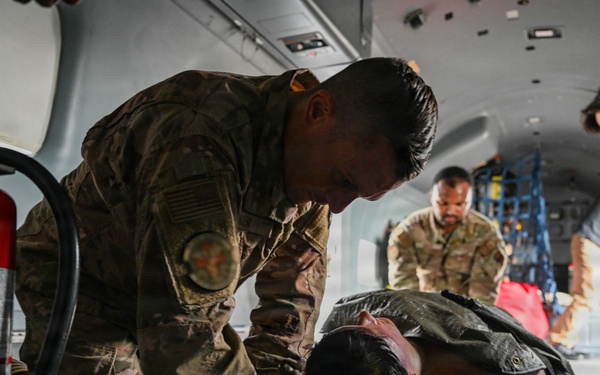 Military personnel in camouflage uniforms are conducting what appears to be a medical evacuation (MEDEVAC) training exercise inside a military aircraft or vehicle. A soldier is attending to a simulated casualty lying on a litter/stretcher on the floor. Additional personnel are visible in the background performing similar tasks.
