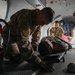 Military personnel in camouflage uniforms are conducting what appears to be a medical evacuation (MEDEVAC) training exercise inside a military aircraft or vehicle. A soldier is attending to a simulated casualty lying on a litter/stretcher on the floor. Additional personnel are visible in the background performing similar tasks.