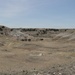 A wide, open semi-arid landscape featuring rolling hills and eroded badlands terrain with sparse vegetation. The valley floor is covered in dry, golden-brown grasses with scattered evergreen trees (likely juniper or cedar) dotting the hillsides and ridgelines. The scene suggests a Great Plains or high plains environment, possibly in states like Nebraska, South Dakota, or Wyoming.