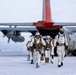 A group of military personnel in white winter camouflage uniforms are disembarking from a military transport aircraft onto a snow-covered surface. The aircraft appears to be a C-130 Hercules variant with a distinctive red tail section and the partial serial number '3049' visible. The scene depicts an arctic or polar military operation, with personnel carrying weapons and tactical gear.