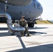 A military service member in OCP (Operational Camouflage Pattern) uniform is performing ground fueling operations on a large military transport aircraft. The aircraft is marked '0177' and '105th AW' (Airlift Wing), identifiable as a C-17 Globemaster III. The service member is crouched near large fuel pipe assemblies connected to an underground fuel pit on a concrete flight line.