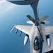 An aerial refueling operation is taking place between a tanker aircraft and an F-16 Fighting Falcon fighter jet at high altitude over a body of water. The tanker's refueling boom is extended and connected to the fighter, which is carrying multiple air-to-air missiles and other ordnance. The tanker is marked with 'PA ANG' indicating it belongs to the Pennsylvania Air National Guard.