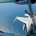An aerial refueling operation is captured from the boom operator's position aboard a tanker aircraft, showing an F-16 Fighting Falcon approaching to receive fuel. The receiver aircraft bears 'PA' and 'ANG' markings, identifying it as belonging to the Pennsylvania Air National Guard. The scene is photographed over a large body of open water visible far below.