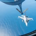 An aerial refueling operation is captured from the boom operator's window of a tanker aircraft, showing an F-16 Fighting Falcon approaching the refueling boom. The tanker's boom is extended downward toward the fighter jet, with 'PA ANG' (Pennsylvania Air National Guard) markings visible on the boom's stabilizing fins. The scene is set over open water or ocean at high altitude.