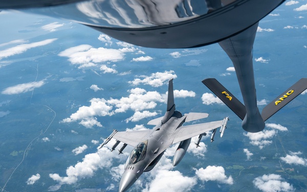 An F-16 Fighting Falcon fighter jet is approaching a KC-135 Stratotanker for aerial refueling at high altitude. The refueling boom of the tanker aircraft is visible in the foreground, marked with 'PA ANG' indicating Pennsylvania Air National Guard. The aircraft are flying over a landscape with scattered cumulus clouds, lakes, and green terrain visible far below.