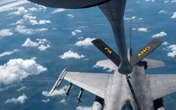 An F-16 Fighting Falcon fighter jet is conducting an aerial refueling operation with a tanker aircraft, visible at the top of the frame. The fighter jet bears markings 'PA' and 'ANG' on its tail fins, indicating it belongs to the Pennsylvania Air National Guard. The aircraft is flying at altitude above scattered cloud cover over what appears to be a rural landscape.
