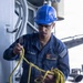A U.S. Navy sailor wearing a blue hard hat and safety glasses is handling a coiled yellow rope on what appears to be the deck of a naval vessel. The sailor's uniform displays 'U.S. NAVY' on the chest along with name patches reading 'LEROY' and rank 'BMSN' (Boatswain's Mate Seaman), assigned to 'MILLER 2ND DIV'. The image captures a routine deck seamanship task aboard a warship.