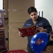 A U.S. Navy sailor named Fernandez is reading a Central Michigan University (CMU) Online brochure at what appears to be an educational fair or recruitment event. The table in the foreground is set up with CMU-branded materials in maroon and gold colors, including brochures, pens, and highlighters. A CMU Online banner is visible to the left, advertising military discounts on tuition.
