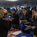 A group of U.S. Navy personnel in dark coveralls and blue hard hats are attending what appears to be an educational or career fair event, likely aboard a naval vessel or facility. Sailors are interacting with a civilian representative at a table displaying materials from what appears to be Texas Southern University (TSU). The event resembles a higher education outreach or benefits fair targeting active-duty military members.