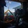U.S. Marines, JMSDF Sailors reinforce maritime readiness during Rescue Flag 26-1 A helicopter rescue operation is underway over open water, with crew members hoisting an injured or incapacitated person on a rescue litter/stretcher into the aircraft. Multiple personnel in flight suits and helmets are coordinating the extraction, with a hoist cable and rigging system visible. The scene appears to be a maritime search and rescue exercise or actual rescue operation, with mountainous coastline visible in the background.