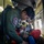 U.S. Marines, JMSDF Sailors reinforce maritime readiness during Rescue Flag 26-1 A rescue personnel wearing a military-style flight suit with a 'Rescue' unit patch is attending to a patient lying on a stretcher inside what appears to be a military or rescue helicopter. The patient is wearing an orange jacket and has an oxygen mask applied to their face. The scene depicts an active aeromedical evacuation or search-and-rescue operation in progress.
