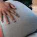 A close-up photograph showing a dark-skinned hand resting on a large woven sack or bag. The hand appears dusty or covered with fine particles, suggesting manual labor. The person is wearing a camouflage-patterned shirt visible in the upper portion of the frame.