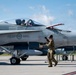 A Royal Canadian Air Force (RCAF) CF-18 Hornet fighter jet with tail number 757 is on an airfield tarmac. Ground crew personnel are conducting pre-flight or post-flight checks while a pilot sits in the cockpit. The aircraft bears the RCAF ARC roundel insignia and crew names 'Cplc Roy' and 'Cpt Ouellet' stenciled on the fuselage.