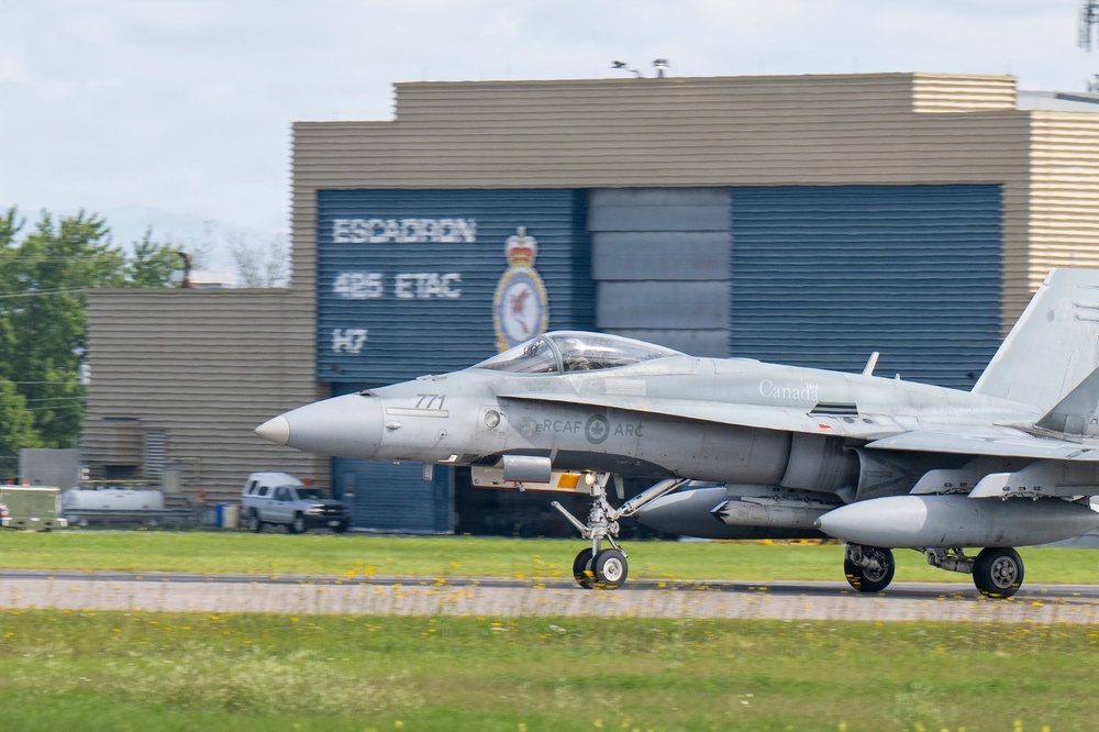 A Royal Canadian Air Force (RCAF) CF-18 Hornet fighter jet with tail number 771 is taxiing on a runway. The aircraft bears 'Canada' and 'RCAF ARC' markings and is photographed in front of a military hangar displaying 'Escadron 425 ETAC 147' signage. The setting appears to be CFB Bagotville or a similar Canadian Forces air base.
