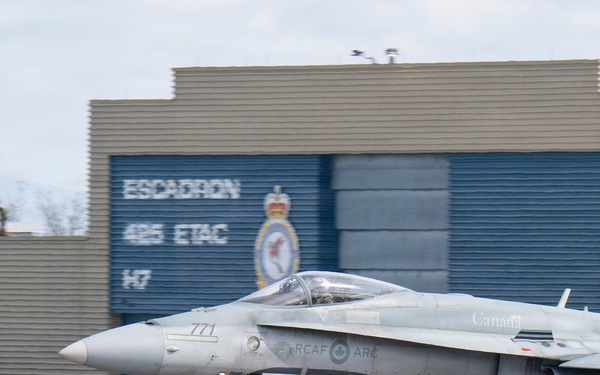 A Royal Canadian Air Force (RCAF) CF-18 Hornet fighter jet with tail number 771 is taxiing on a runway. The aircraft bears 'Canada' and 'RCAF ARC' markings and is photographed in front of a military hangar displaying 'Escadron 425 ETAC 147' signage. The setting appears to be CFB Bagotville or a similar Canadian Forces air base.
