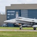 A Royal Canadian Air Force (RCAF) CF-18 Hornet fighter jet with tail number 771 is taxiing on a runway. The aircraft bears 'Canada' and 'RCAF ARC' markings and is photographed in front of a military hangar displaying 'Escadron 425 ETAC 147' signage. The setting appears to be CFB Bagotville or a similar Canadian Forces air base.