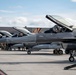 A line of F-16 Fighting Falcon jet fighters are parked on a flight line apron, with canopies open and pilots seated in cockpits. The aircraft bear 'AC' tail codes and markings consistent with the New Jersey Air National Guard's 177th Fighter Wing based at Atlantic City Air National Guard Base. Ground crew personnel are visible performing pre-flight or maintenance activities alongside the aircraft.