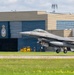 An F-16 Fighting Falcon jet fighter is captured during takeoff or landing on a runway, with its landing gear still deployed. The aircraft bears the tail code 'AC' and serial number '345', indicating it belongs to the New Jersey Air National Guard's 177th Fighter Wing. In the background, a Canadian military hangar marked 'ESCADRON 425 ETAC' is visible, suggesting this is a joint or exchange operation at a Canadian Forces base.