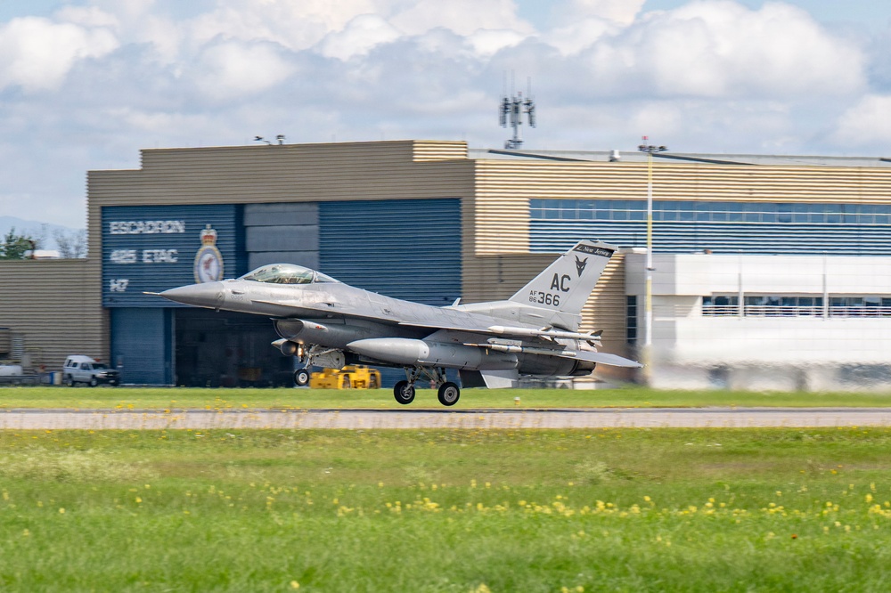 A U.S. Air Force F-16 Fighting Falcon (tail code AC, serial AF 85-366) is captured during takeoff or landing roll on a runway. The aircraft is in front of a Canadian military hangar marked 'Escadron 425 ETAC' with a Royal Canadian Air Force insignia visible. The setting appears to be a joint or visiting operation at a Canadian Forces base.