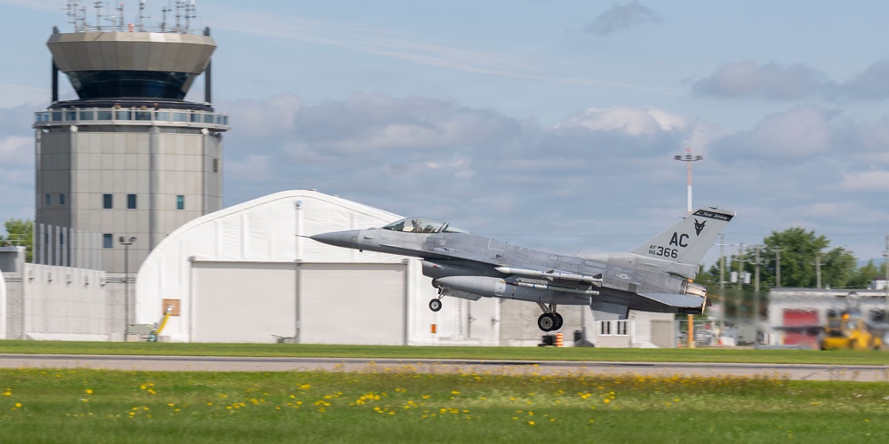 An F-16 Fighting Falcon fighter jet with tail code 'AC 366' and markings indicating AF 86 is captured during takeoff or landing on a runway. The aircraft bears 'New Jersey' state markings on the tail fin, suggesting it belongs to the New Jersey Air National Guard. An air traffic control tower and a white aircraft hangar are visible in the background.