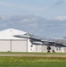An F-16 Fighting Falcon fighter jet with tail code 'AC 366' and markings indicating AF 86 is captured during takeoff or landing on a runway. The aircraft bears 'New Jersey' state markings on the tail fin, suggesting it belongs to the New Jersey Air National Guard. An air traffic control tower and a white aircraft hangar are visible in the background.