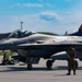 A U.S. Air Force F-16 Fighting Falcon assigned to the 119th Fighter Squadron, New Jersey Air National Guard, sits on a flight line tarmac with tail number AF 86-309, nicknamed 'Jersey Jerk.' A ground crew member stands at attention in front of the aircraft while a pilot is visible in the cockpit. The tail fin features the distinctive orange and blue New Jersey Air National Guard markings with 'AC 119FS' designation.