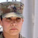 A close-up portrait of a female U.S. Army soldier wearing Operational Camouflage Pattern (OCP) uniform and patrol cap. A Staff Sergeant rank insignia is visible on the front of her cap. She has a serious, composed expression and is photographed against a blurred outdoor background.