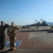 Three U.S. Air Force personnel are saluting a T-38 Talon jet aircraft on a flight line tarmac. The aircraft bears 'U.S. AIR FORCE' markings and tail code 'RA' with partial number '14' visible, with at least one occupant visible in the cockpit. This appears to be a formal military ceremony, likely a solo flight, final flight, or departure ceremony.