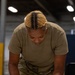 A female military service member in OCP (Operational Camouflage Pattern) uniform is leaning over a table, reviewing documents in what appears to be a warehouse or hangar facility. She is holding a yellow highlighter and appears to be actively marking or reviewing paperwork. The image is a close-up, professionally composed photograph with sharp focus on the subject.