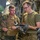 Air Force, Marines conduct joint training on C-17 Two military personnel are reviewing documents or a tablet inside what appears to be a military aircraft cargo hold. The individual on the left is wearing USMC MARPAT camouflage with a plate carrier vest, while the individual on the right wears an olive drab t-shirt with MultiCam trousers and tactical gloves. They appear to be conducting a briefing, inspection, or load planning review.
