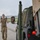 Air Force, Marines conduct joint training on C-17 A military service member in multicam/OCP uniform and black gloves is directing a military vehicle on what appears to be an airfield tarmac. A second service member is visible in the side mirror reflection of the green military tactical vehicle. The scene suggests a ground marshaling or vehicle movement operation.