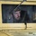 Air Force, Marines conduct joint training on C-17 A soldier wearing a military helmet is visible through the windshield of a desert-tan colored military Humvee (HMMWV). The vehicle's exterior is painted in a sand/tan color typical of desert operations. A notepad and what appears to be a red pen or marker are visible on the dashboard inside the vehicle.