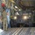 Air Force, Marines conduct joint training on C-17 A military HMMWV (Humvee) is being loaded or unloaded from a large military transport aircraft, likely a C-17 Globemaster III, as indicated by the distinctive cargo bay interior. At least two personnel are visible inside the Humvee while a third soldier in MultiCam/OCP uniform guides the vehicle from the side. The vehicle's headlights are illuminated and the surface appears wet, suggesting recent rain or washing.