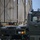 Air Force, Marines conduct joint training on C-17 A military vehicle operator in sunglasses is seated in the cab of an olive-drab military truck, maneuvering or positioning large tan military containers secured with chains on flatbed trailers. The containers bear a red 'FLAMMABLE' hazard diamond placard, indicating hazardous cargo. The scene appears to be a military logistics or loading operation, likely at an airfield or staging area.