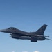 A single-seat F-16 Fighting Falcon jet fighter is photographed in flight against a clear blue sky. The aircraft bears tail code 'AC' and serial number '324', indicating it belongs to the New Jersey Air National Guard's 177th Fighter Wing based at Atlantic City. The aircraft is carrying external stores including what appear to be fuel tanks and air-to-air missiles.