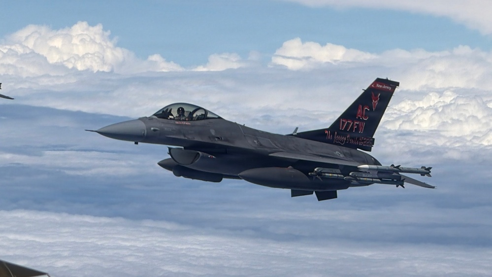 A U.S. Air Force F-16 Fighting Falcon jet fighter is photographed in flight above a cloud layer. The aircraft belongs to the 177th Fighter Wing (177FW) of the New Jersey Air National Guard, identifiable by the distinctive black and red tail markings with 'AC' tail code. The aircraft is armed and flying in formation, photographed from a nearby aircraft.