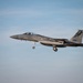 A U.S. Air Force F-15 Eagle fighter jet is captured in flight with landing gear fully extended, indicating an approach or landing phase. The aircraft bears tail markings 'AF 86-165' and the word 'CALIFORNIA,' identifying it as belonging to the California Air National Guard. The image is taken against a clear blue sky with minimal cloud cover.