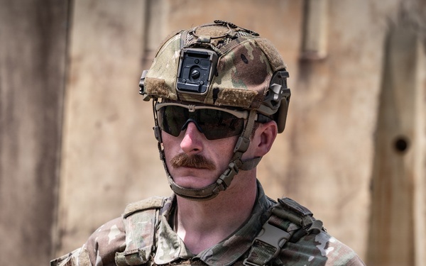 A U.S. Air Force service member identified as 'Morris' is photographed in full tactical gear including a multicam combat uniform, plate carrier vest, and ballistic helmet with mounted device. The individual appears to be in a deployed or operational environment based on the arid background setting. The image is a professional close-up portrait-style photograph emphasizing the service member's equipment and insignia.